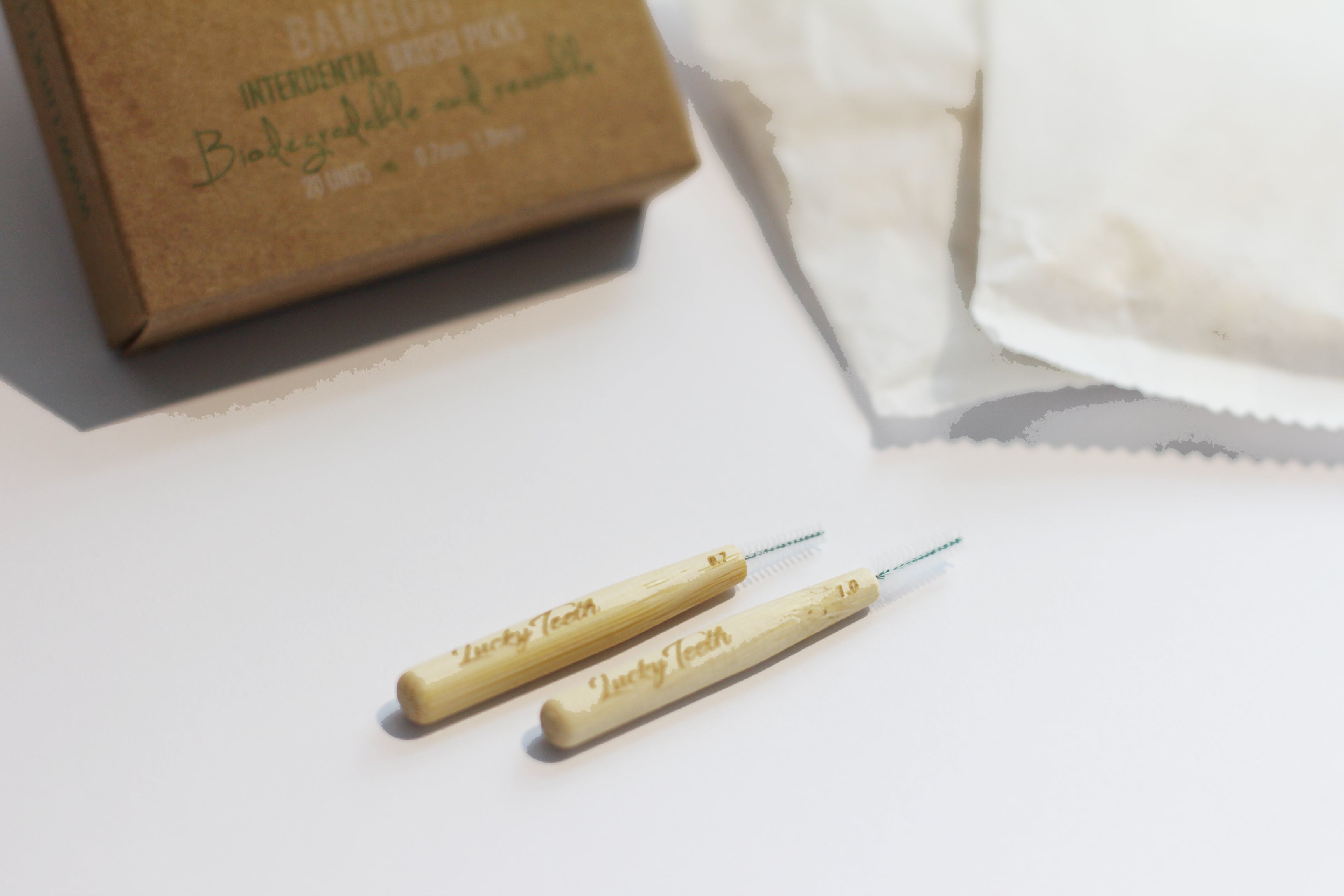 Two wooden teethers on a white surface with a brown box labeled 'Baby's First' in the background.