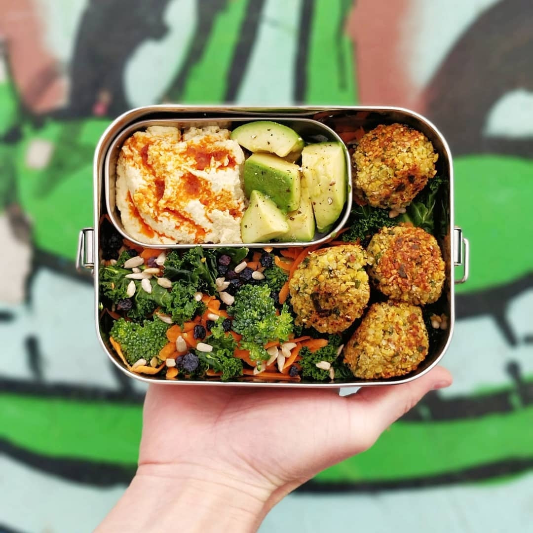 Hand holding a bento box with a variety of food items against a colorful background