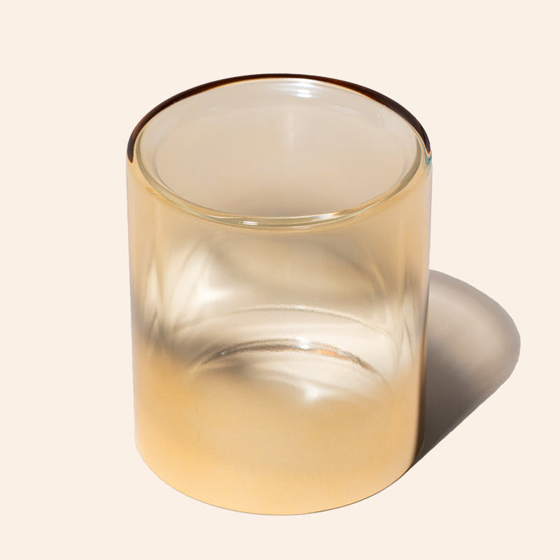 Clear glass candle holder with a warm tint on a beige background