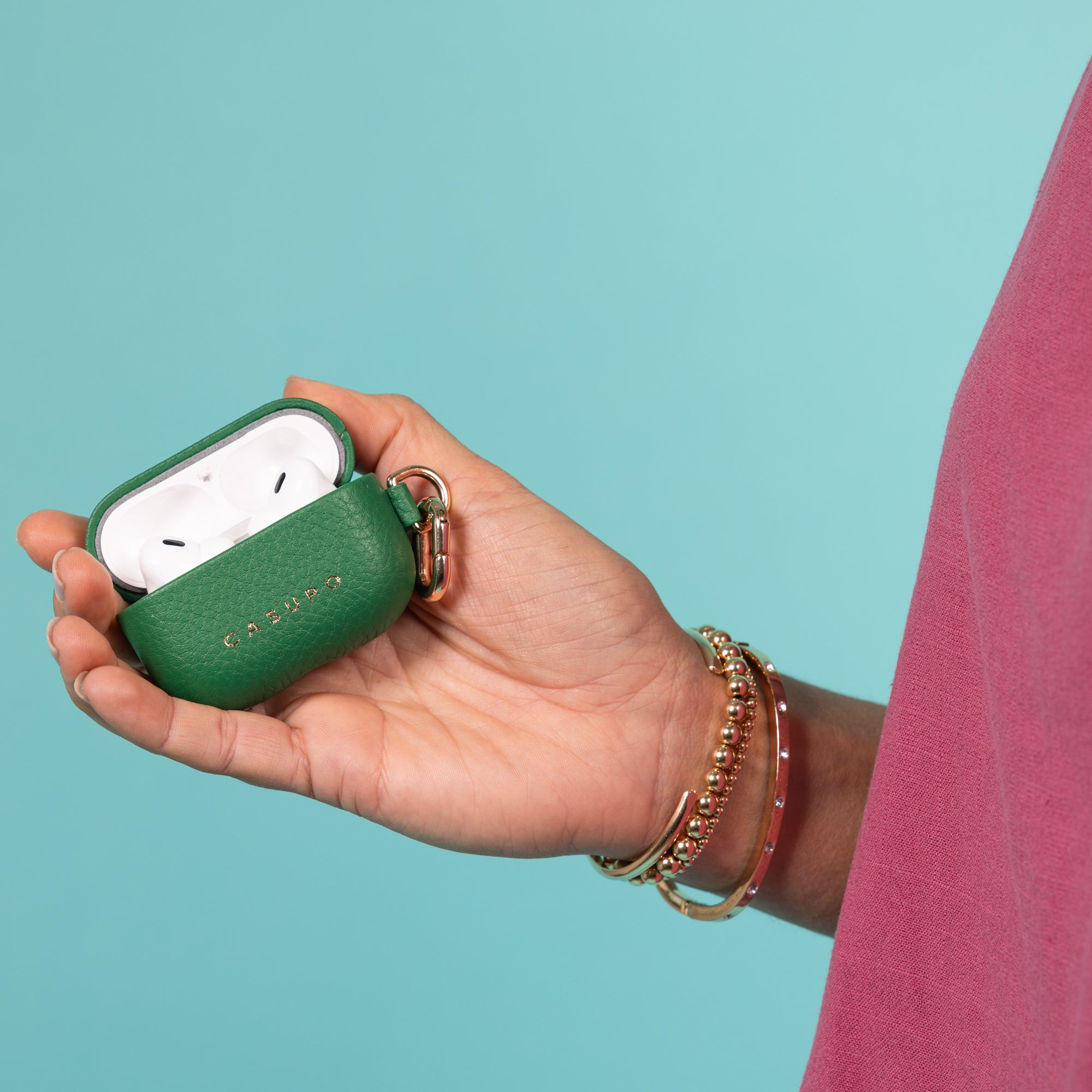 Hand holding a green AirPods case against a teal background