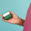 Hand holding a green AirPods case against a teal background