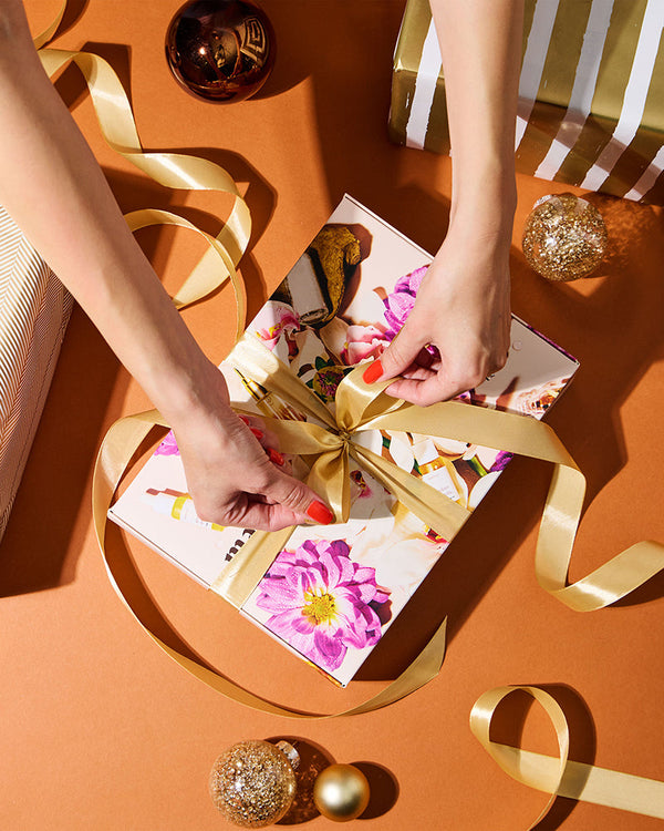 Person tying a gold ribbon on a gift with decorative elements on an orange surface