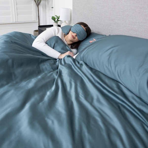 Person lying in bed with blue bedding and a matching eye mask.