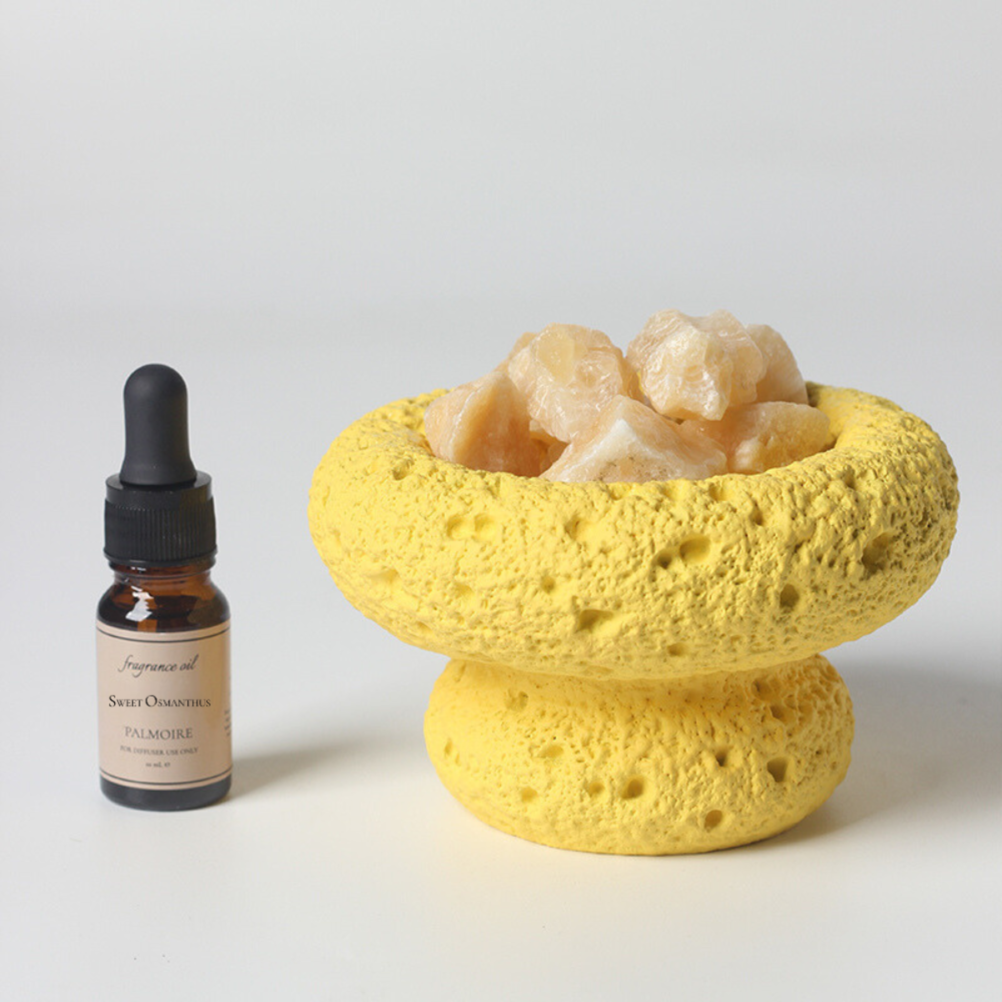 Yellow sponge bowl with scallops and a bottle of fragrance oil on a light background