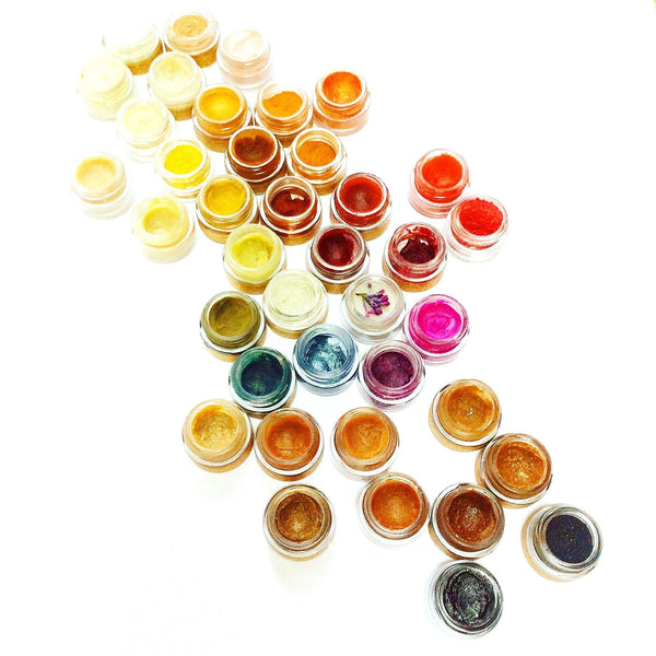 Assorted small jars of colorful substances arranged in a heart shape on a white background