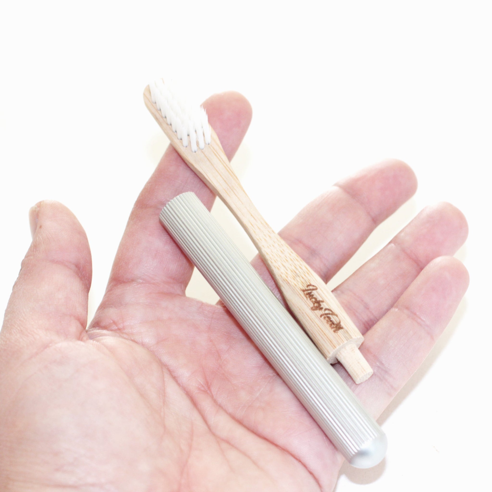 Hand holding a metal toothbrush and a wooden toothbrush with 'Vegan Love' branding on a white background