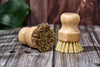 Desesh bamboo dish scrubbing brush resting on plastic-free paper packaging on a wooden surface