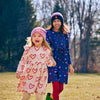 Two children in colorful dresses and hats standing in a park.