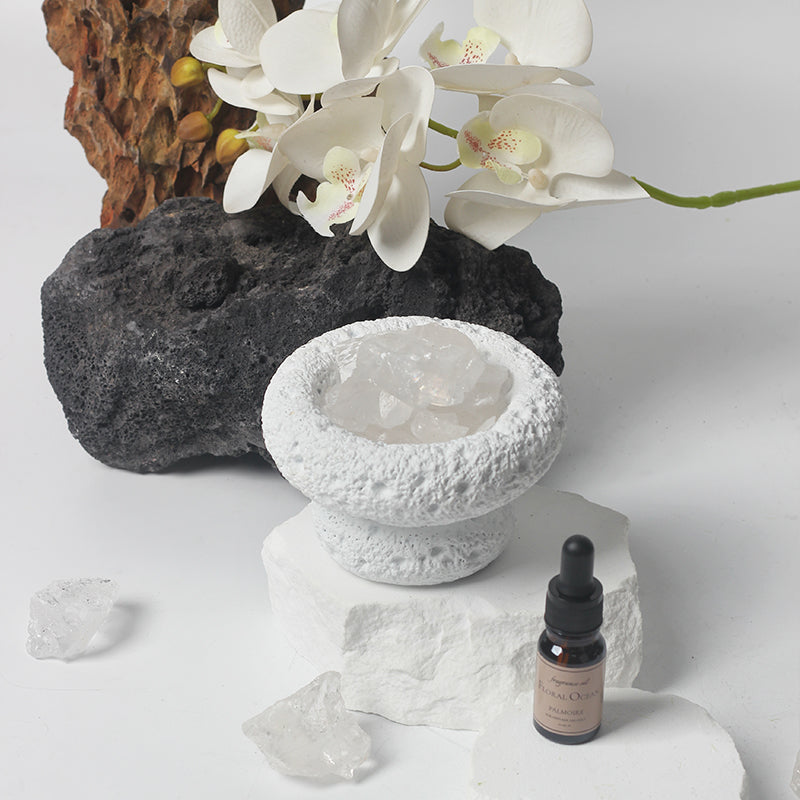 Ceramic bowl with crystals, white orchids, and a bottle on a light background