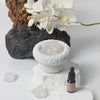 Ceramic bowl with crystals, white orchids, and a bottle on a light background