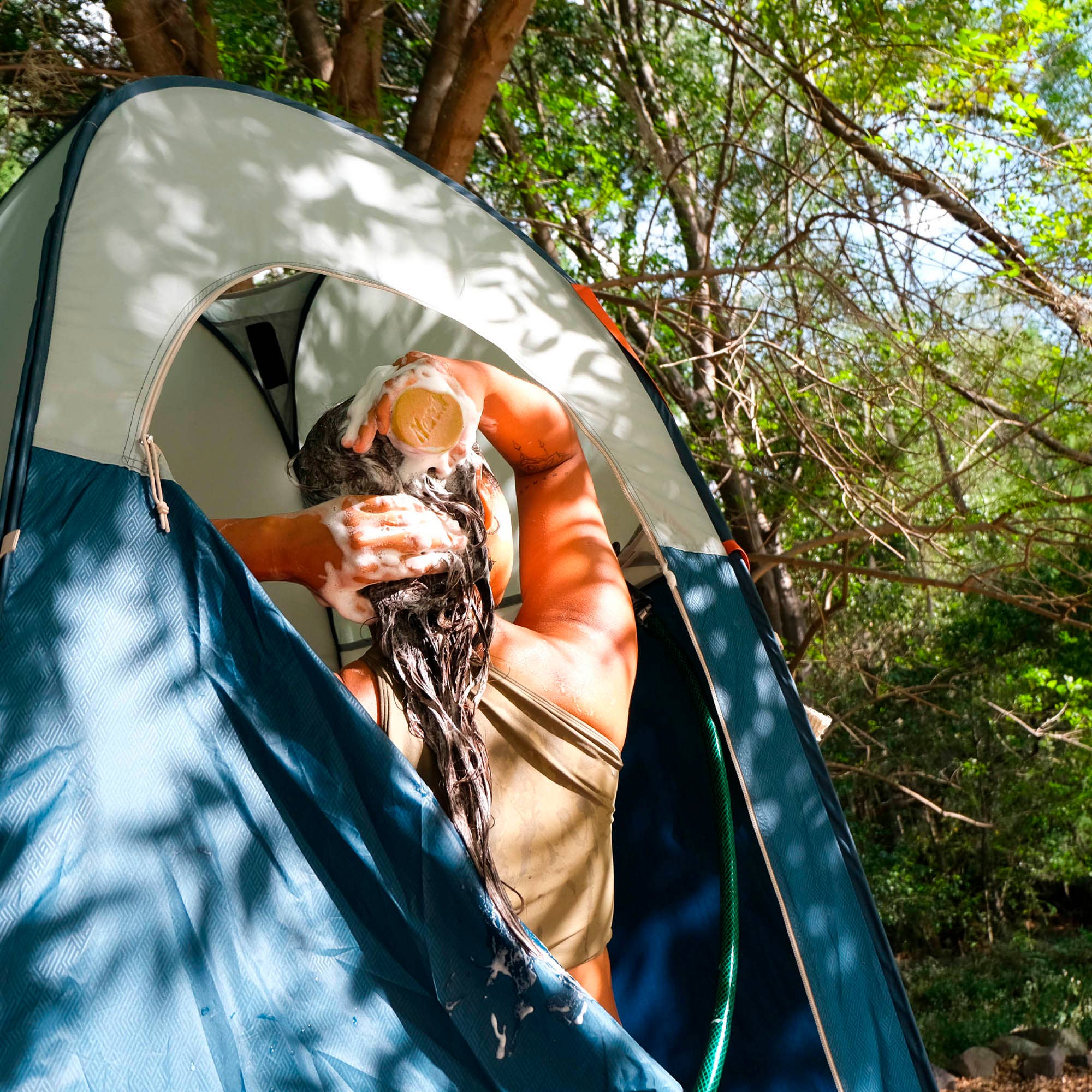 Person washing hair inside a tent in a forest setting