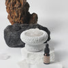 Decorative stone bowl with a bottle of essential oil on a white background