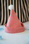 Red and white checkered Santa hat with a pom-pom on a striped background