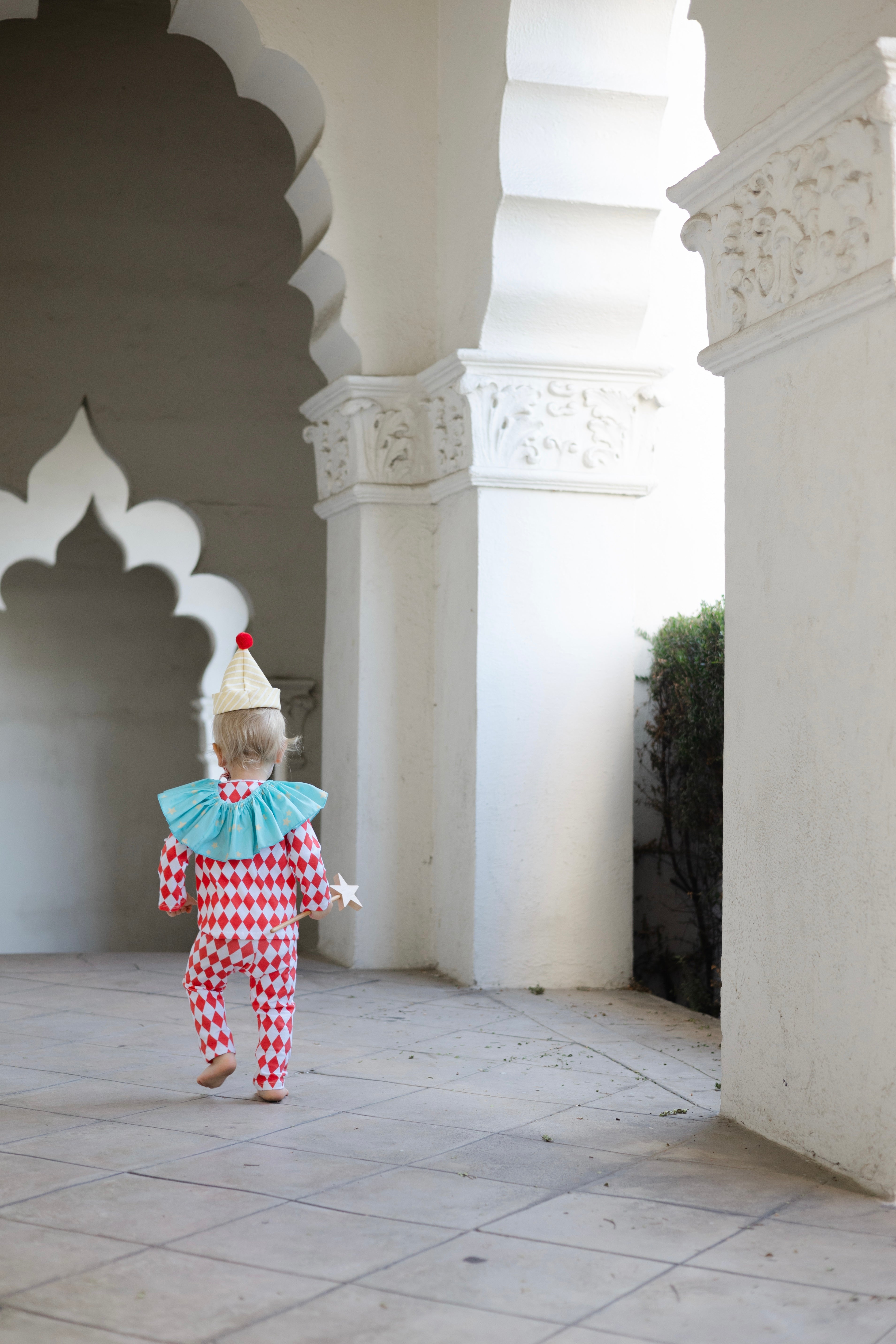 Child in clown costume walking through a sunlit architectural courtyard