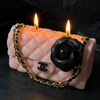 Candle shaped like a Chanel handbag with a black rose and gold chain, lit on a dark background.