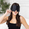 Woman wearing a black satin eye mask against a white background
