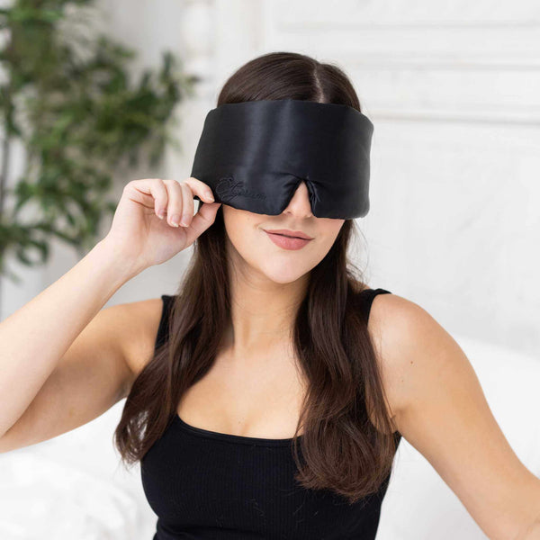 Woman wearing a black satin eye mask against a white background