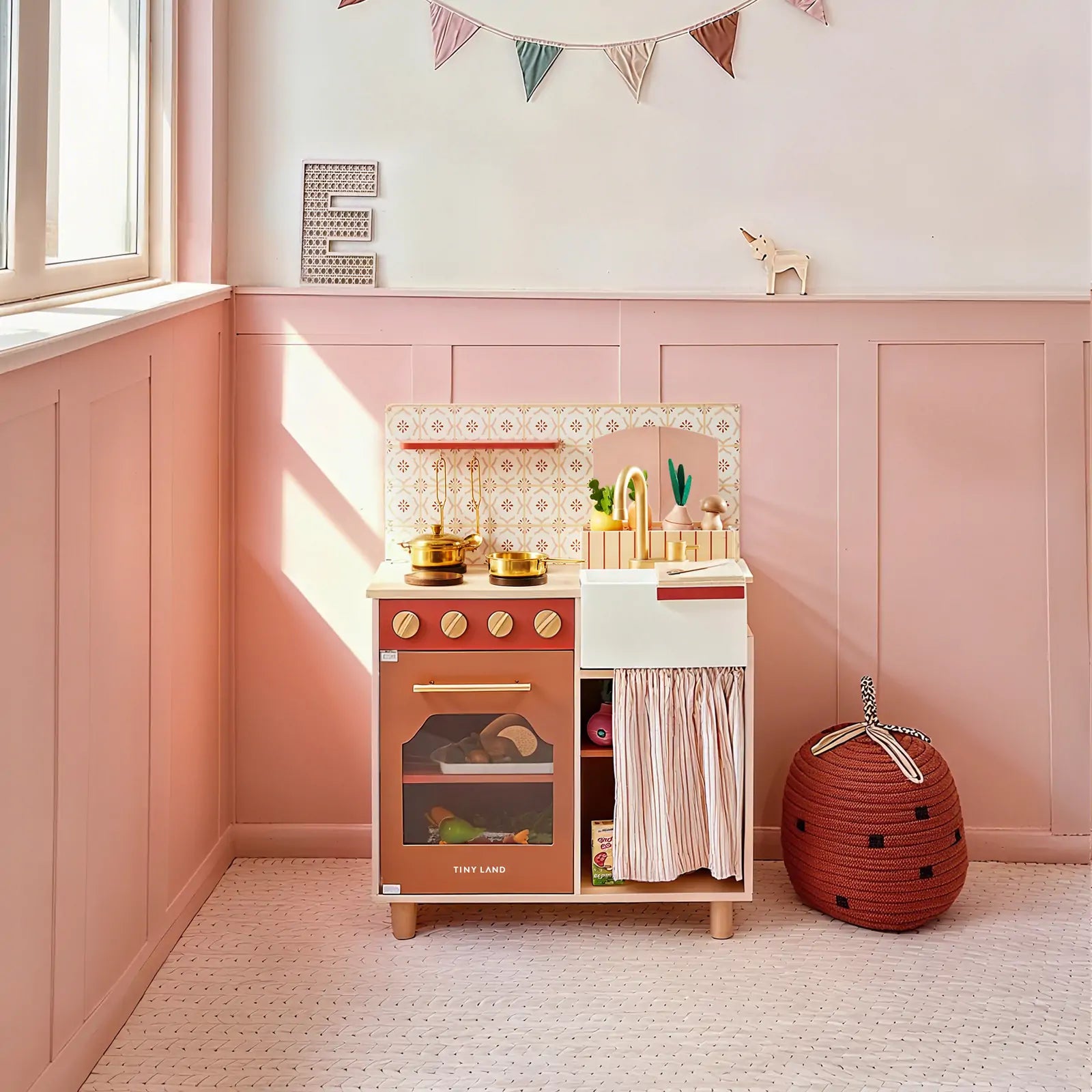 Children's play kitchen set against a pink wall with decorative elements.