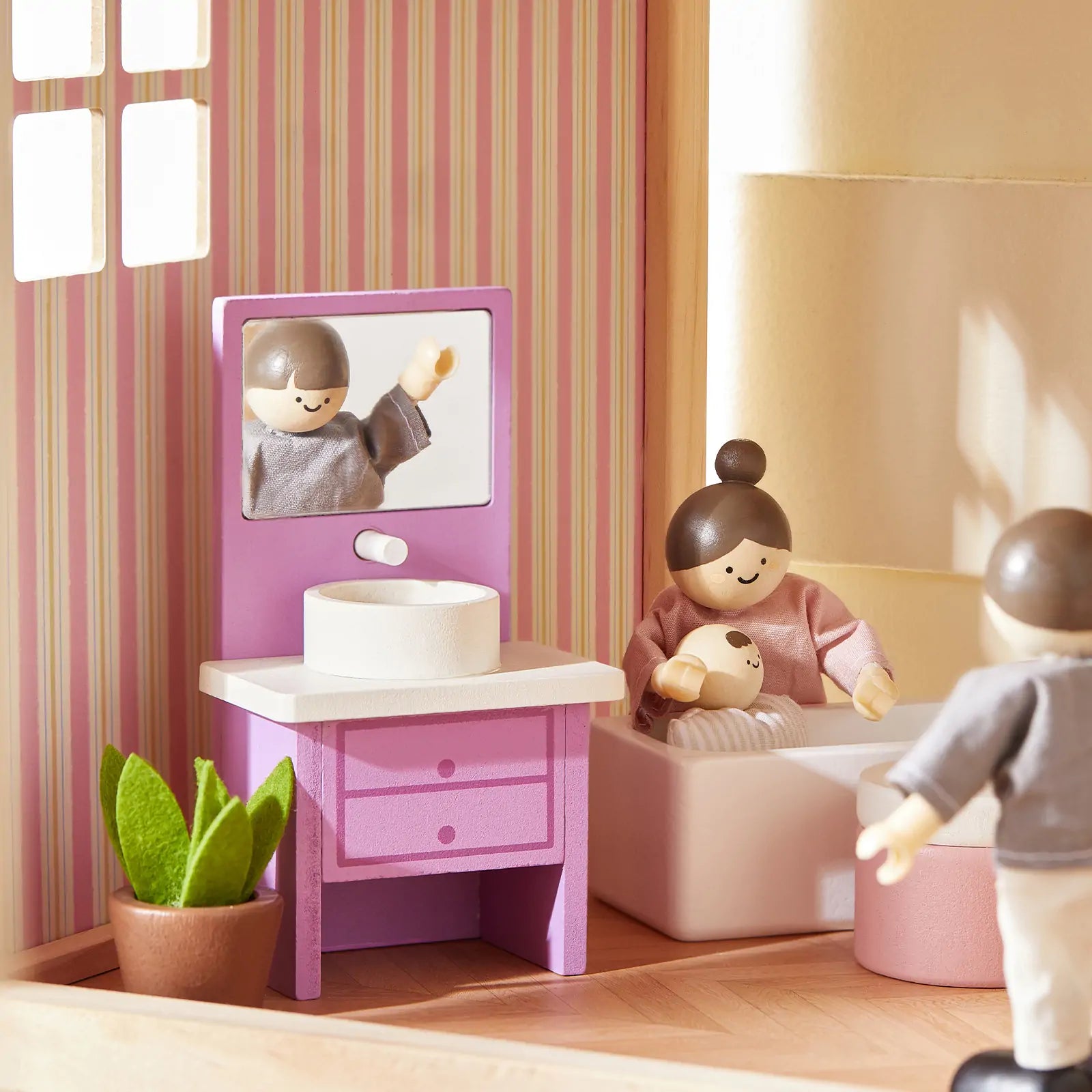 Toy setup with a pink vanity, mirror, and dolls in a room with striped wallpaper.