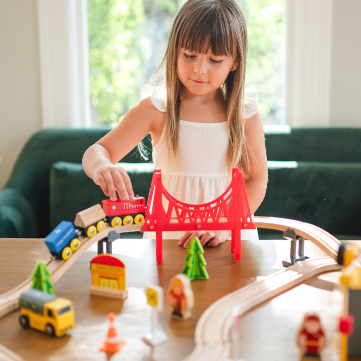 Young girl playing with a toy train set on a table.
