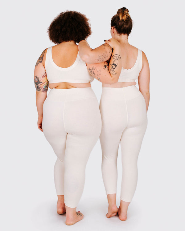Two people wearing matching white outfits standing back-to-back on a plain background