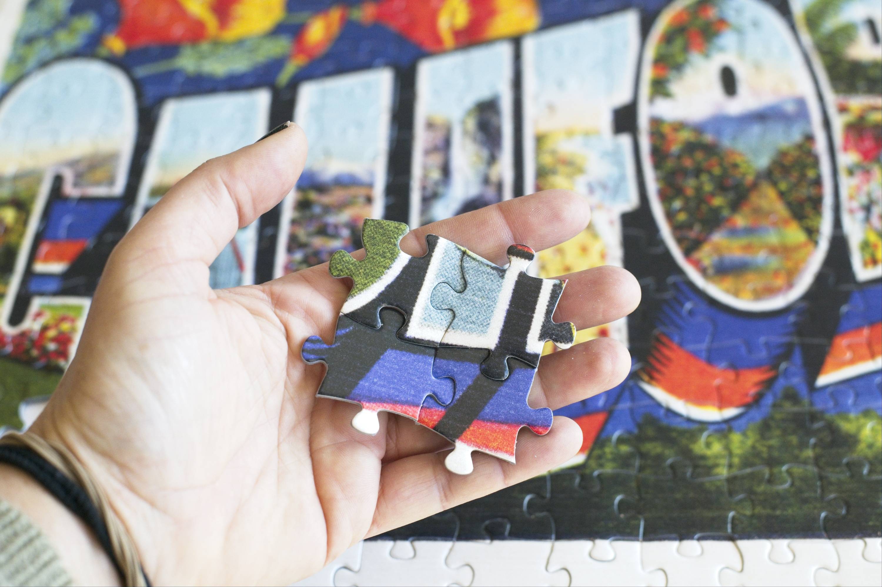 300-piece jigsaw puzzles from Oakland Puzzle Company with puzzle pieces held in a hand