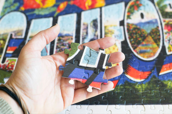 300-piece jigsaw puzzles from Oakland Puzzle Company with puzzle pieces held in a hand