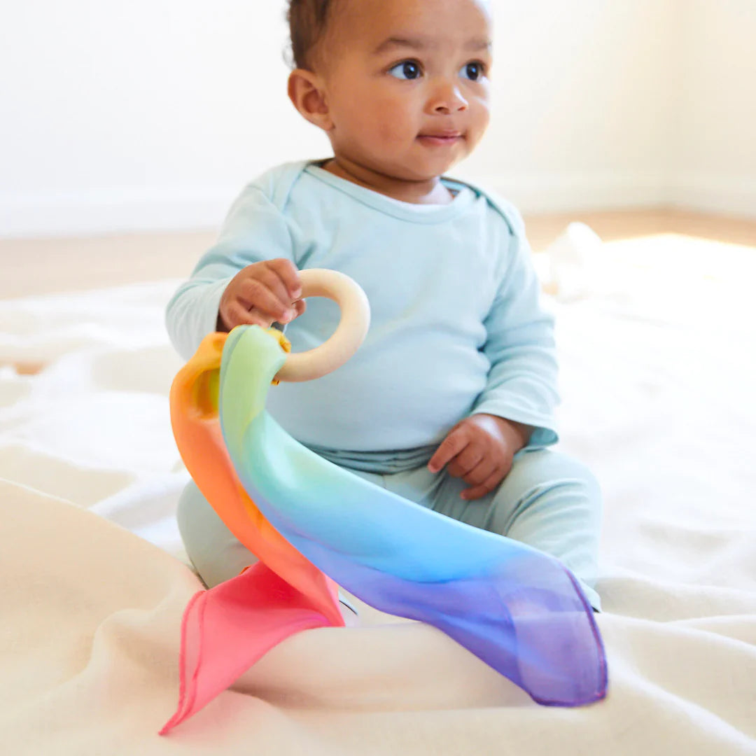 Baby holding the Sarah's Silks Rainbow Teether, showing the easy-grip Maple wood ring and silk playsilk