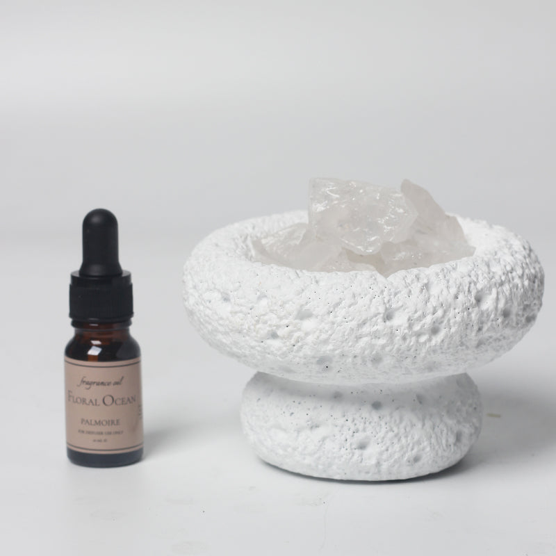 Bottle of 'Floral Ocean' perfume next to a textured white ceramic bowl on a light gray background
