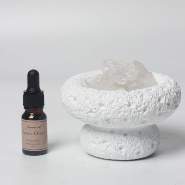 Bottle of 'Floral Ocean' perfume next to a textured white ceramic bowl on a light gray background