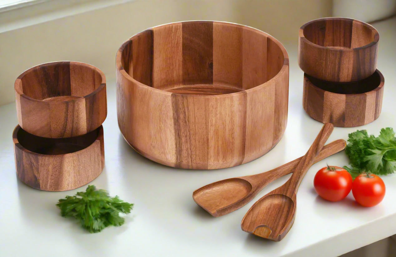 Set of wooden kitchen utensils including a bowl, cups, and spoons on a white surface with vegetables.