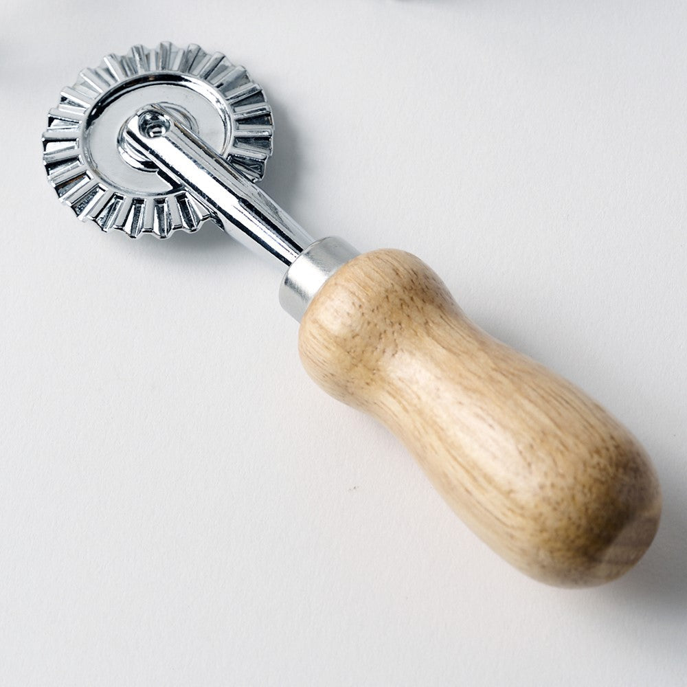 Dough roller with wooden handle and metal wheel on a white background