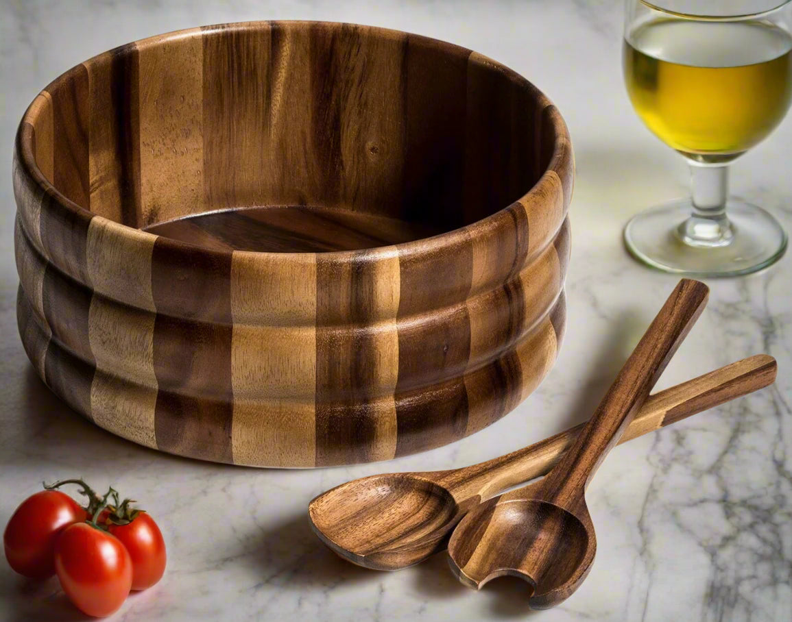 Wooden salad bowl with two wooden spoons and cherry tomatoes on a marble surface.