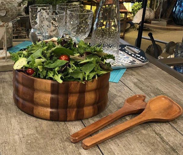 Wooden salad bowl with fresh greens and tomatoes on a rustic wooden table.