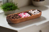 Wooden snack tray with compartments filled with various snacks on a light surface.