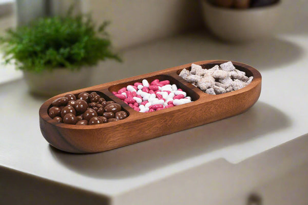 Wooden snack tray with compartments filled with various snacks on a light surface.