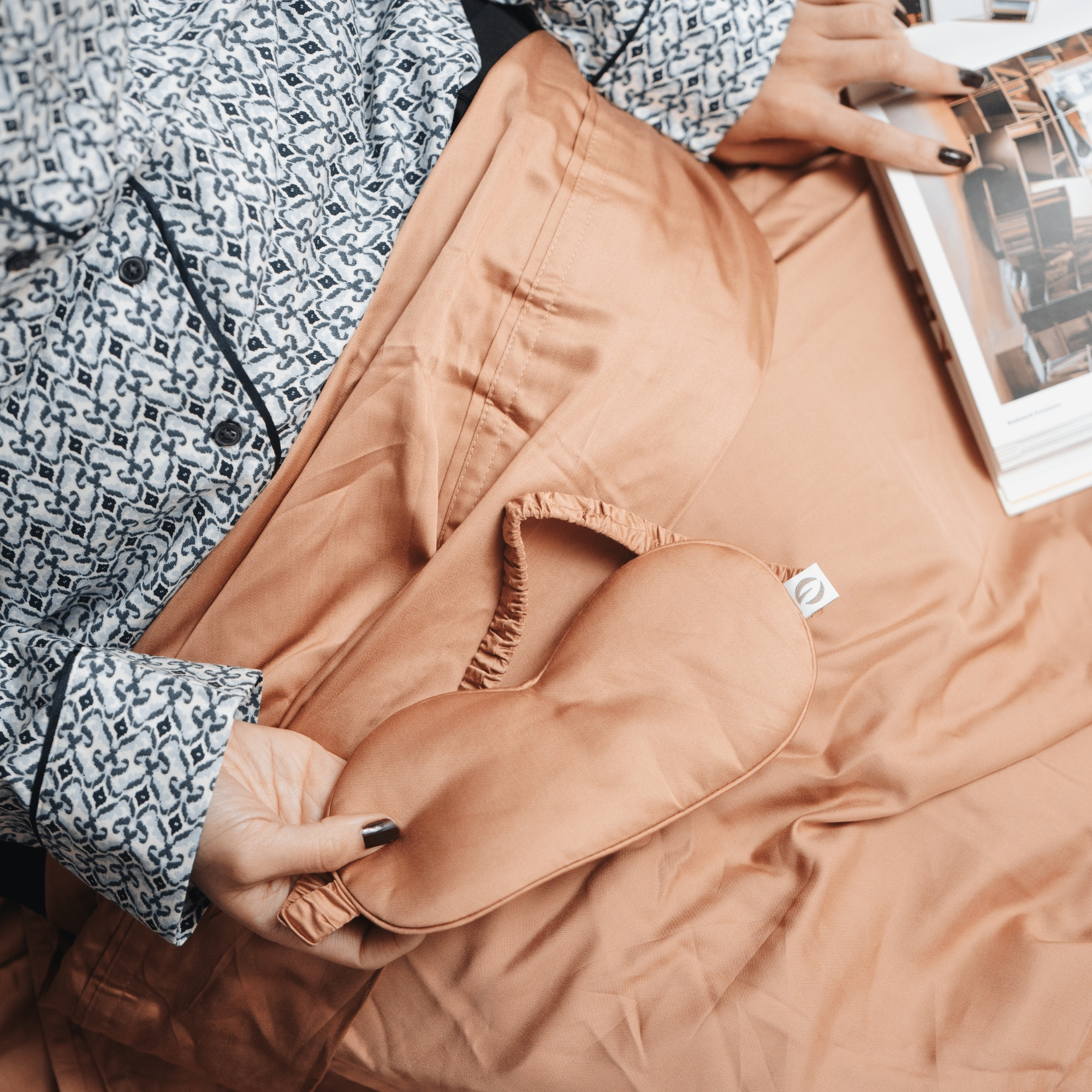 Person wearing a patterned shirt and holding a brown jacket with a visible brand logo.