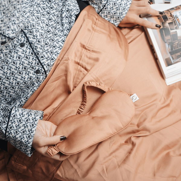 Person wearing a patterned shirt and holding a brown jacket with a visible brand logo.