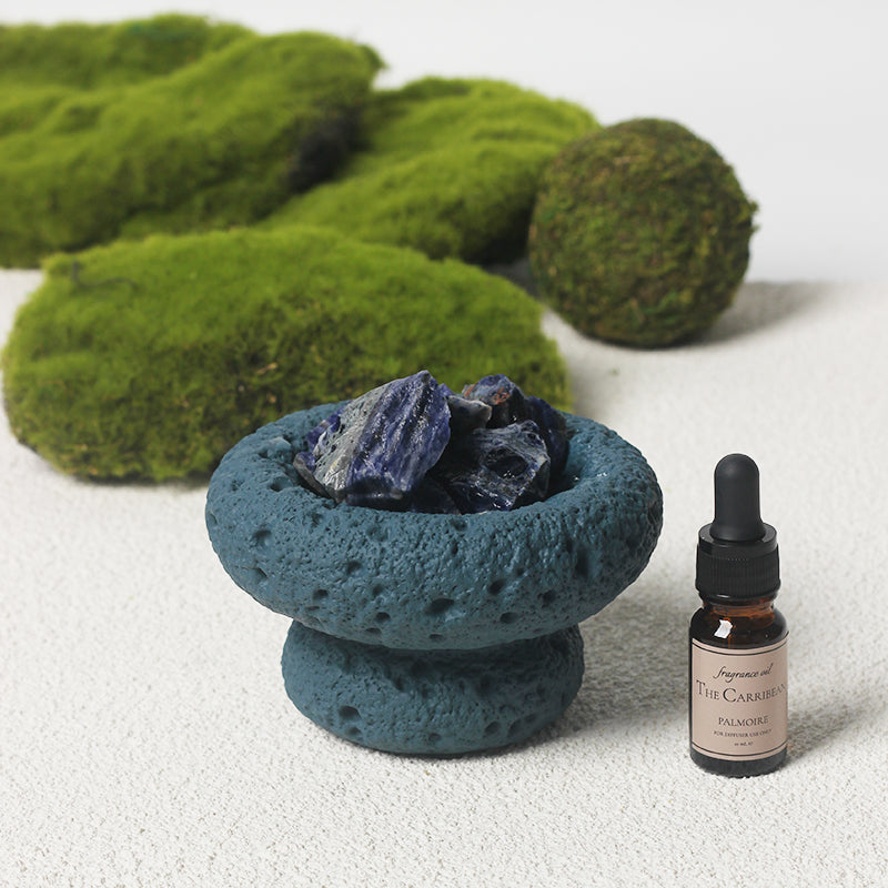 Blue stone bowl with blue stones and a bottle of essential oil on a white background
