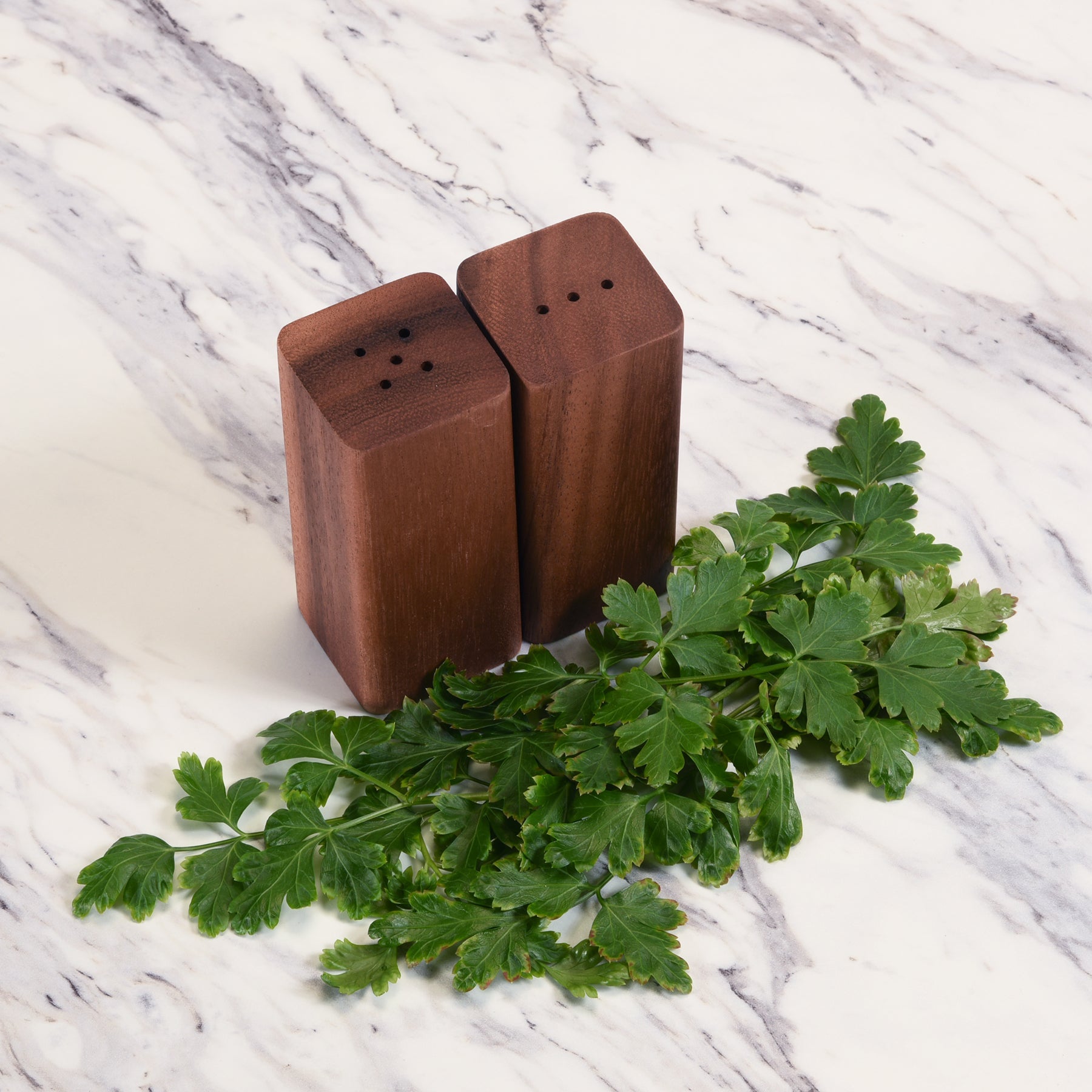 Wooden salt and pepper shakers with green herbs on a marble surface