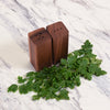 Wooden salt and pepper shakers with green herbs on a marble surface
