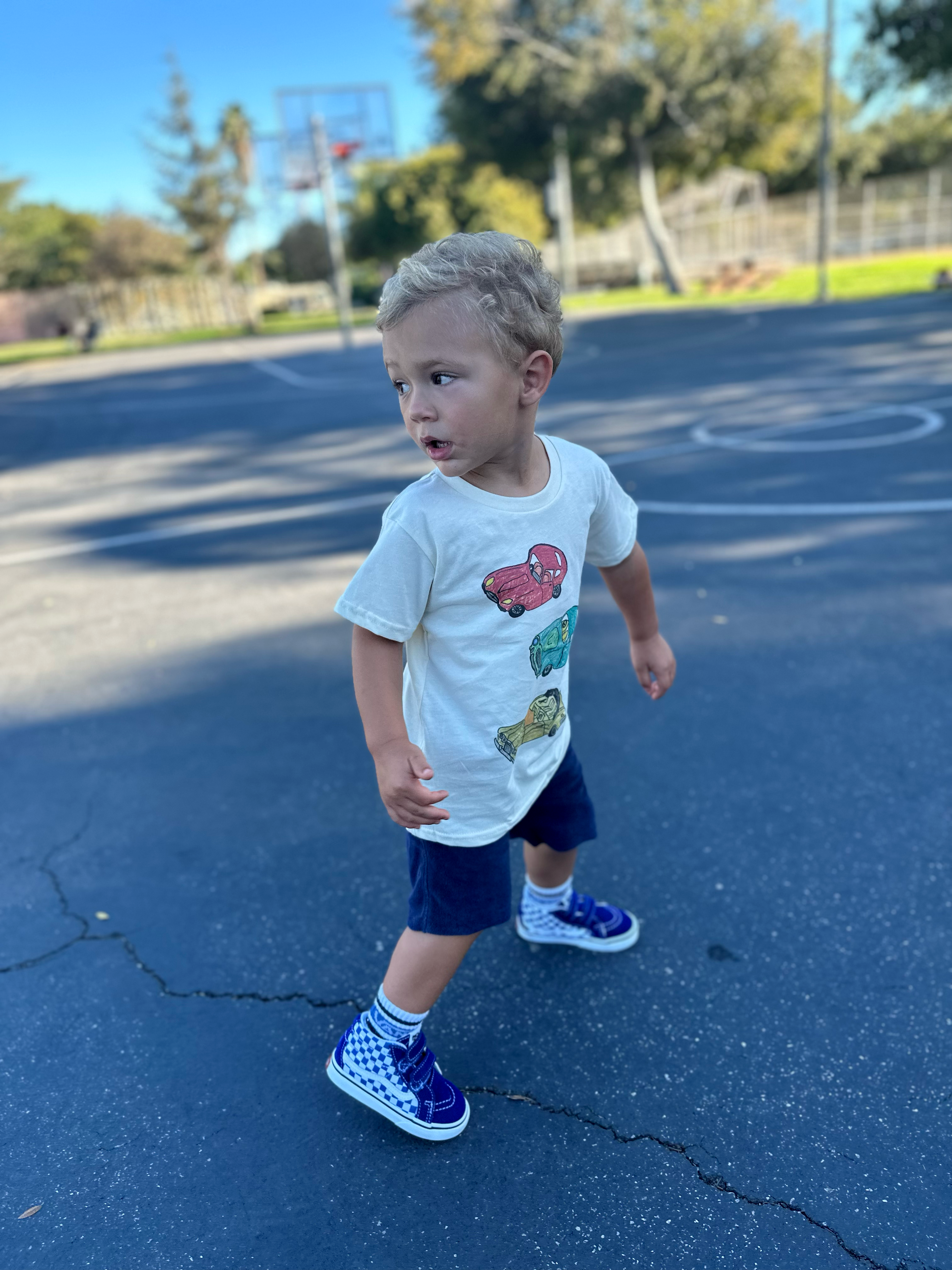 Child standing on a blue playground surface with trees and a clear sky in the background