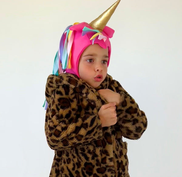 Child wearing a leopard print onesie with a colorful unicorn hood and gold horn.