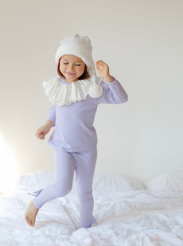 Child wearing a lavender outfit with a white ruffled collar and matching hat on a white background