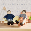 Two wooden dolls sitting on a couch with a rocking horse against a decorative wall.