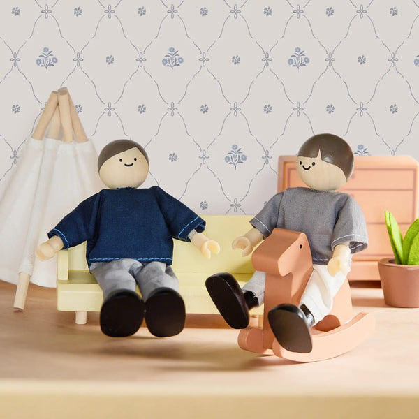 Two wooden dolls sitting on a couch with a rocking horse against a decorative wall.
