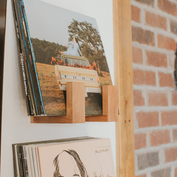 Stack of vinyl records on a wooden record holder against a brick wall.