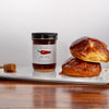 Jar of hot honey with a honey dipper and pastries on a white surface.