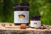 Two jars of cacao and honey on a wooden surface with a blurred green background