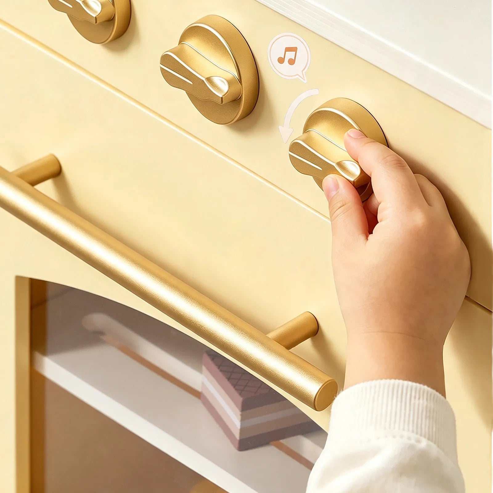 A close-up of a hand turning a gold control knob on a cream-colored toy or appliance, with a music icon graphic near the knob.